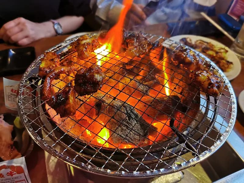 Potongan daging sapi dipanggang di atas panggangan arang dengan api menyala di meja restoran