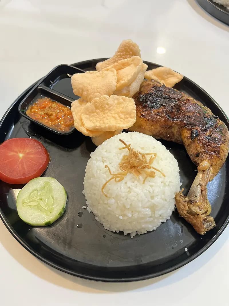 Nasi ayam bakar madu: paha ayam bakar kecokelatan dengan nasi putih, sambal, kerupuk, tomat, dan timun