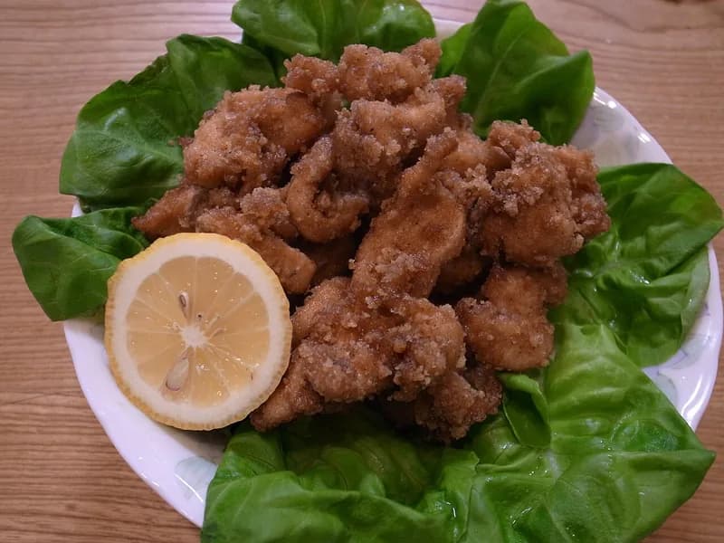 Potongan ayam goreng berbumbu bawang putih dan jahe berbalut tepung renyah di atas daun selada dengan irisan lemon