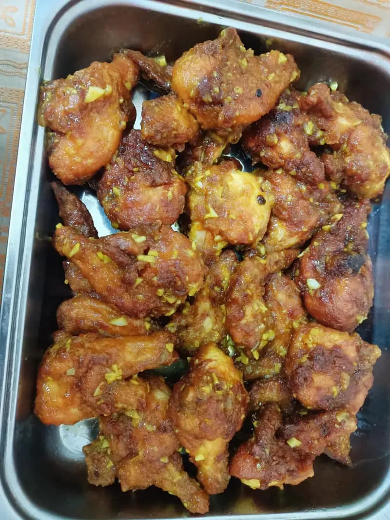 Potongan ayam goreng berbalut saus mentega dan cincangan bawang putih di wadah saji stainless
