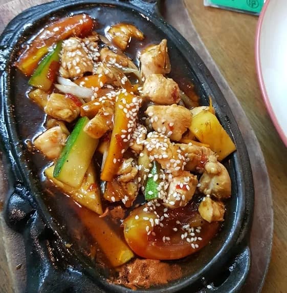 Ayam lada hitam di hot plate dengan saus cokelat kental, wortel, zukini, dan taburan wijen