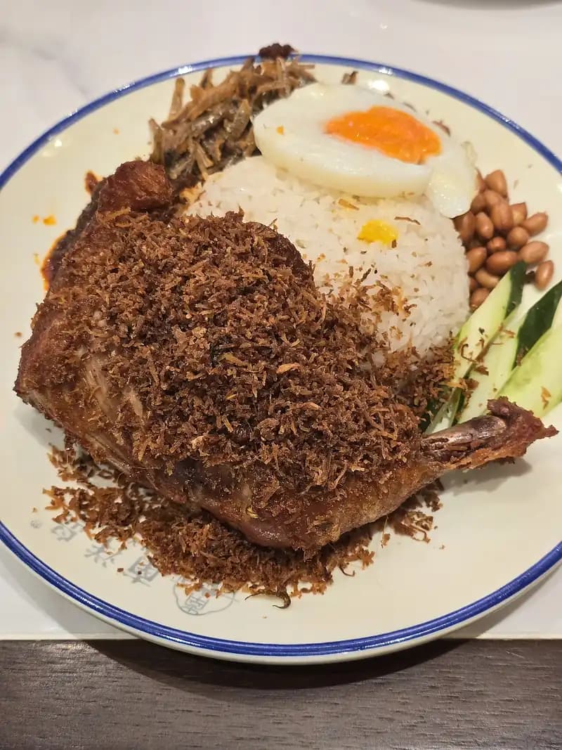 Paha ayam goreng bertabur serundeng kelapa cokelat dengan nasi putih, telur mata sapi, kacang, dan timun