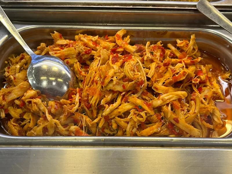 Ayam suwir rica-rica pedas dengan cabai merah cincang di wadah saji stainless dan sendok sayur