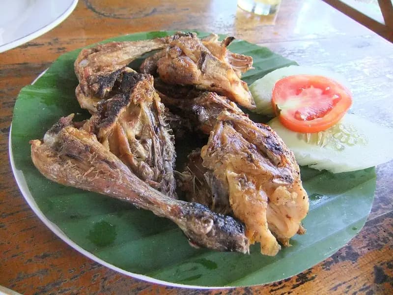 Potongan ayam bakar taliwang di Lombok di atas daun pisang dengan irisan tomat dan mentimun