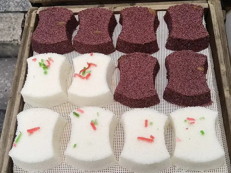 Kue kukus beras hitam berwarna ungu tua bertekstur berpori berjajar di samping kue beras putih
