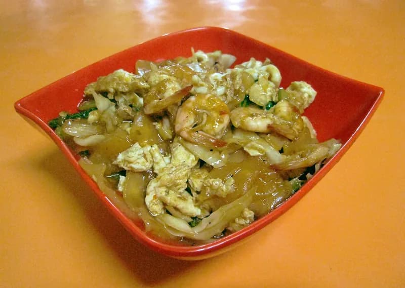 Semangkuk seblak seafood berisi kerupuk basah, udang, telur orak-arik, dan sawi dalam mangkuk merah