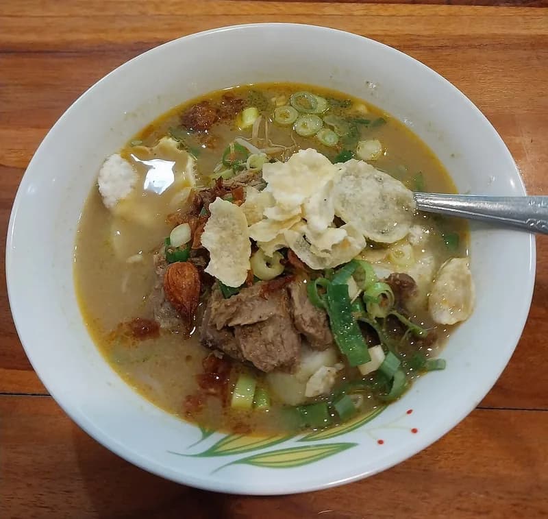 Semangkuk empal gentong berkuah santan kuning dengan daging sapi, kerupuk, dan irisan daun bawang