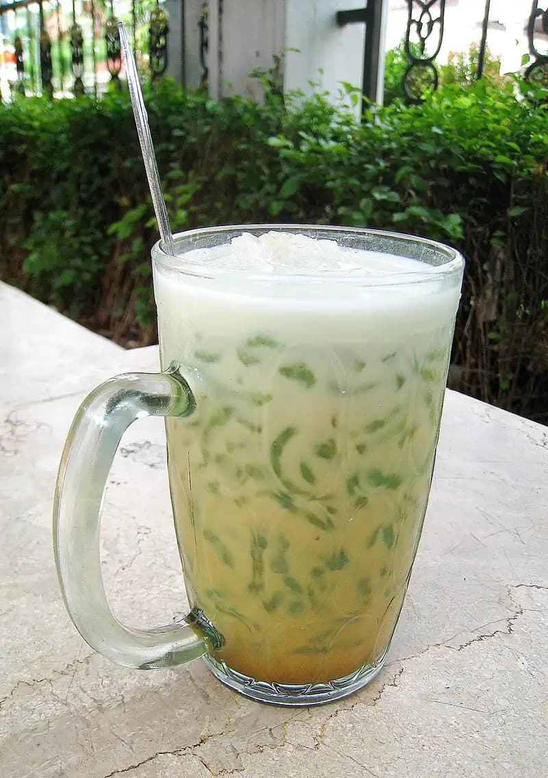Segelas es cendol dengan cendol hijau, santan putih, dan gula merah cair di dasar gelas
