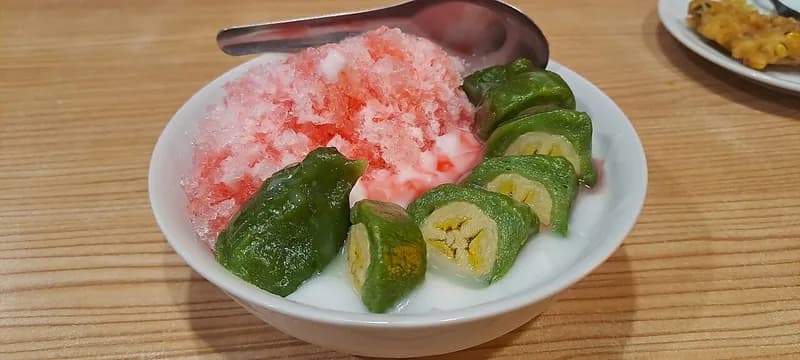Semangkuk es pisang ijo berisi potongan pisang berbalut adonan hijau, es serut merah, dan saus santan