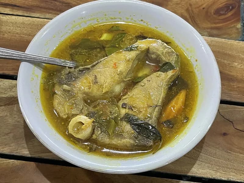 Semangkuk ikan kuah kuning berisi potongan ikan, daun kemangi, dan tomat dalam kuah kunyit