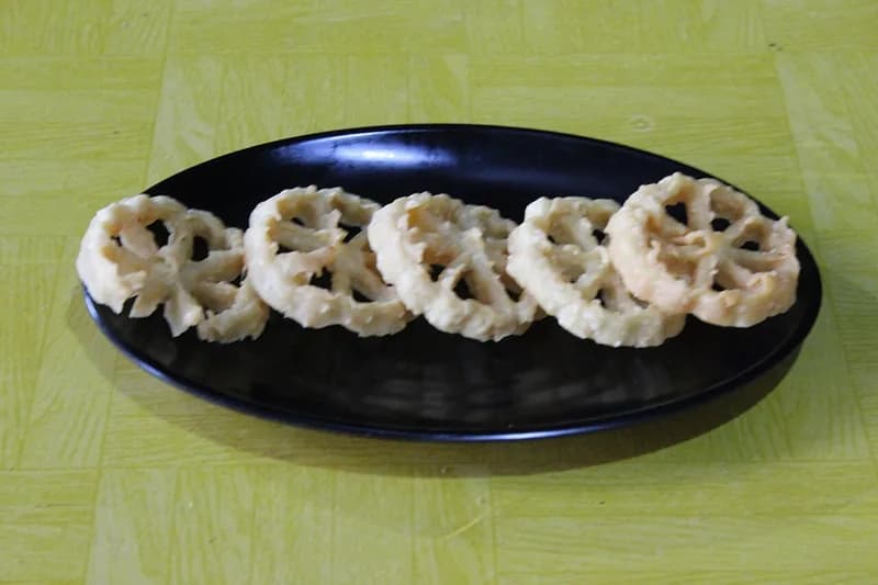 Lima keping kue kembang goyang Betawi berwarna krem berjajar di atas piring hitam