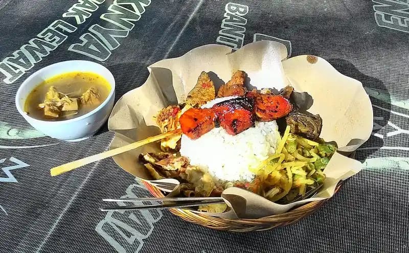 Nasi campur Bali dalam keranjang anyaman beralas kertas dengan sate, daging panggang, sayur berbumbu, dan semangkuk sup