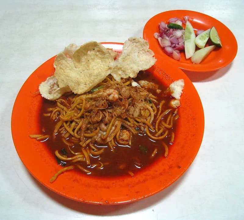 Sepiring mie Aceh berkuah merah pedas dengan udang dan emping, ditemani acar bawang merah