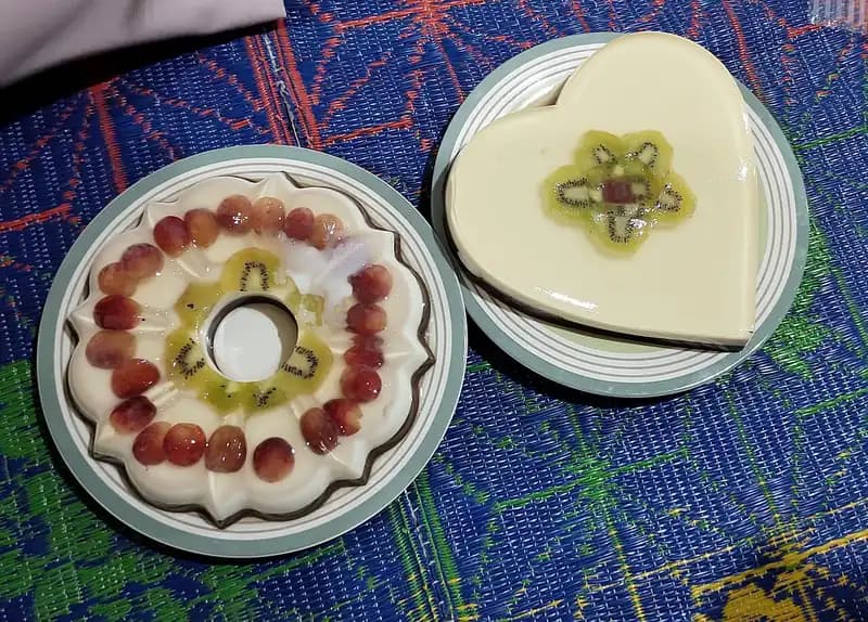 Dua puding susu cetakan bundar dan hati berhias anggur merah dan irisan kiwi