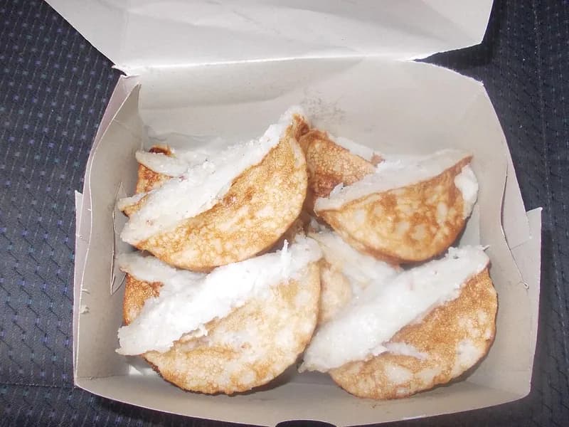Kue pancong setengah lingkaran berbahan kelapa parut dengan bagian bawah kecokelatan dalam kotak kertas