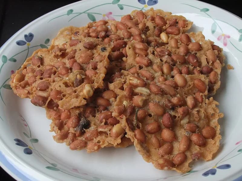 Beberapa lembar peyek kacang tanah renyah berwarna keemasan di atas piring bermotif bunga