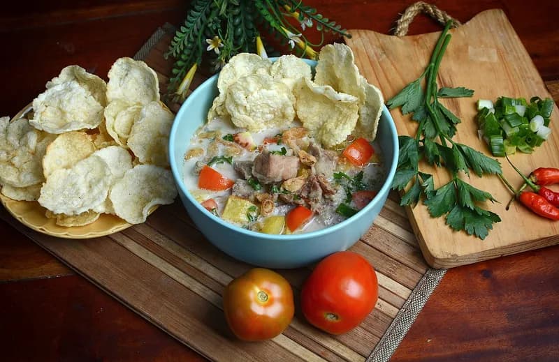 Semangkuk soto betawi berkuah santan dengan daging sapi, tomat, kentang, dan emping melinjo