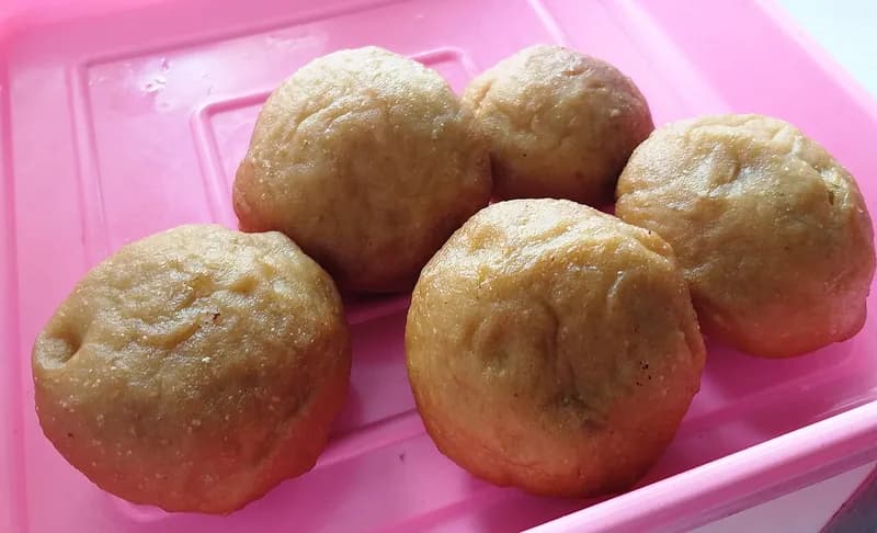 Lima roti goreng bulat berwarna cokelat keemasan isi unti kelapa di wadah plastik merah muda