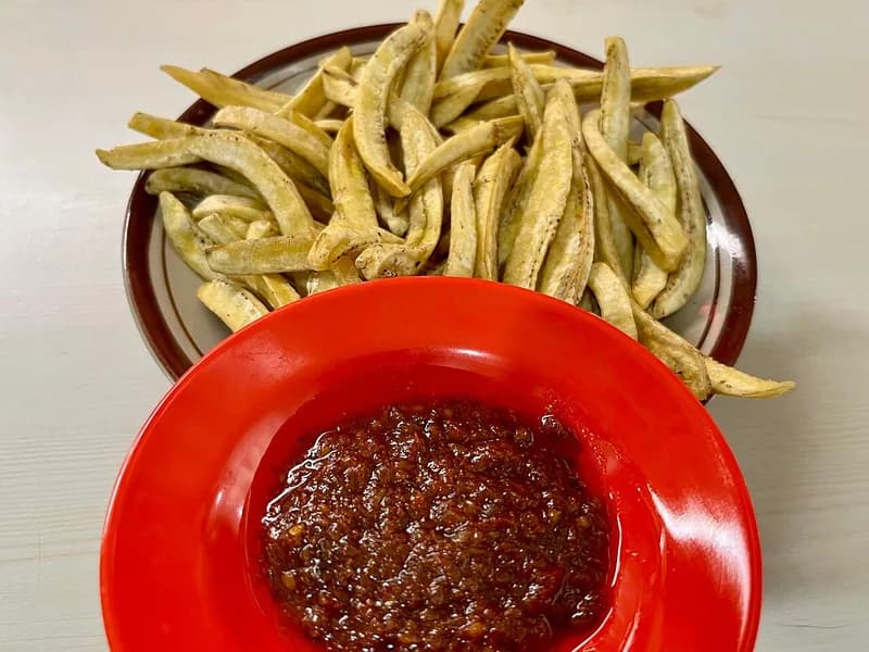 Sambal roa merah kecokelatan di piring merah dengan keripik pisang goroho khas Manado