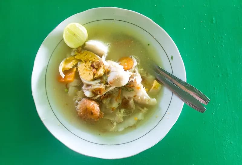 Semangkuk soto Banjar berkuah bening dengan suwiran ayam, telur rebus, perkedel, wortel, dan jeruk nipis