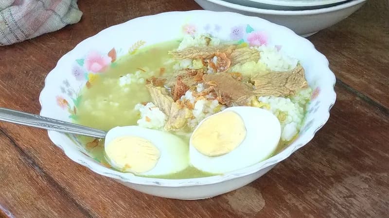 Semangkuk soto Madura daging sapi berkuah kuning bening dengan nasi, telur rebus, dan bawang goreng