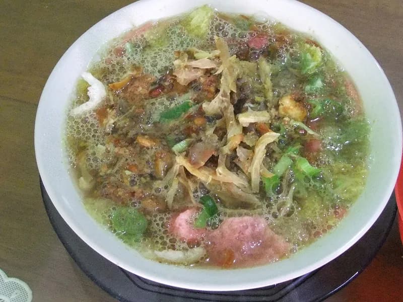 Semangkuk soto Sokaraja dengan suwiran ayam, kerupuk merah muda, ketupat, daun bawang, dan sambal kacang di kuahnya
