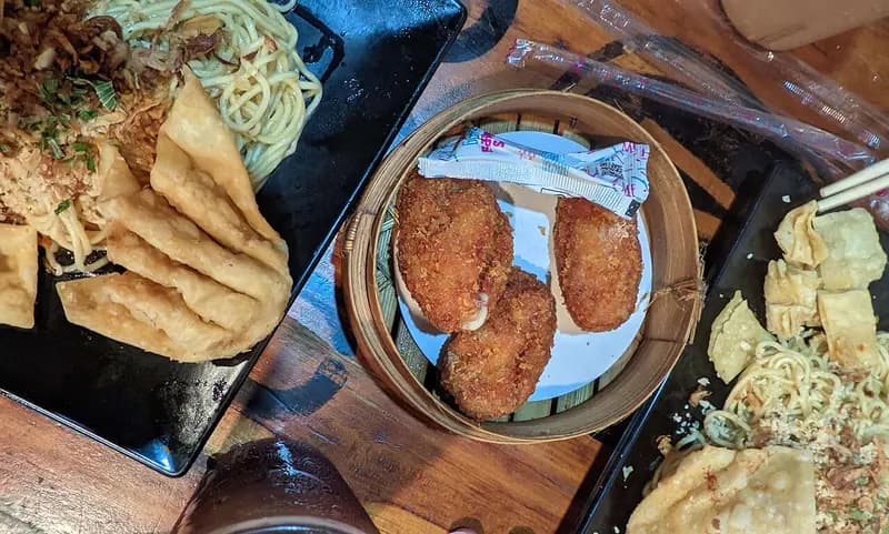 Tiga potong udang keju goreng tepung renyah di kukusan bambu, diapit mi dan pangsit goreng