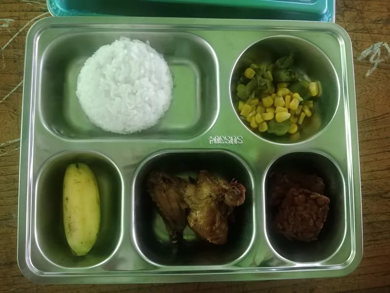 Nampan makan sekolah berisi nasi putih, tumis jagung dan buncis, ayam goreng, tempe, dan pisang