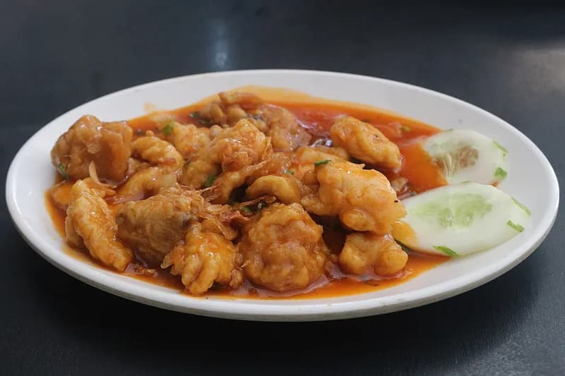 Sepiring ayam asam manis goreng tepung berlumur saus merah dengan irisan timun