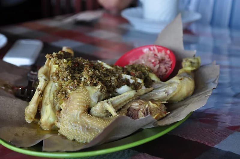Ayam betutu utuh berlumur bumbu base genep di atas kertas nasi dengan sambal matah