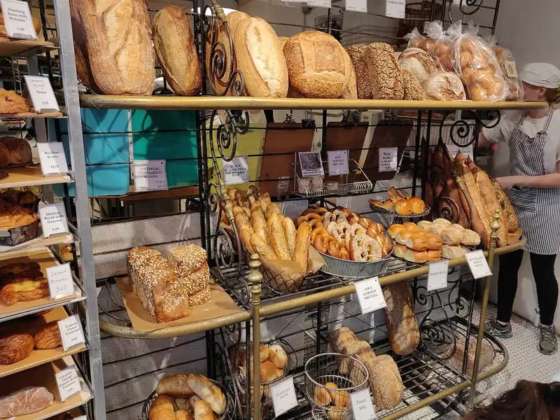 Rak besi bakery penuh roti sourdough, baguette, bagel, dan roti manis dengan papan nama harga