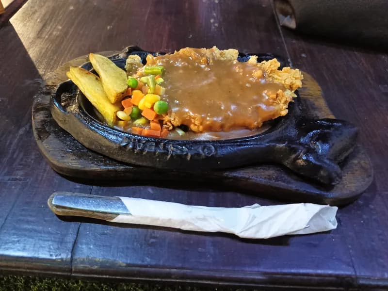 Steak ayam bersaus cokelat di hot plate dengan kentang goreng dan sayuran wortel, jagung, buncis