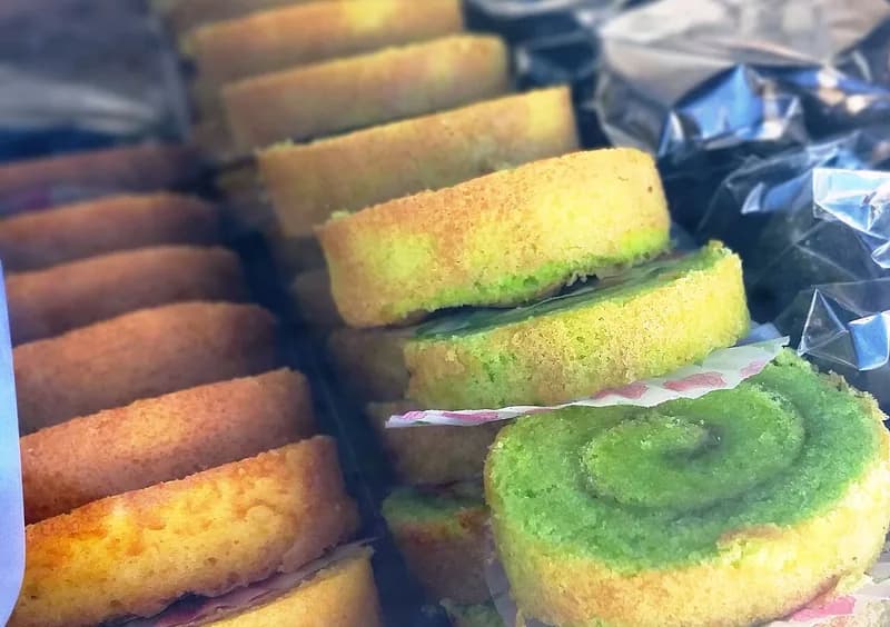 Irisan bolu gulung pandan berwarna hijau dengan pola spiral tersusun berjajar di etalase