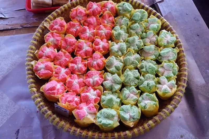 Tampah bambu berisi puluhan bolu kukus mekar warna merah muda dan hijau dalam cup kertas