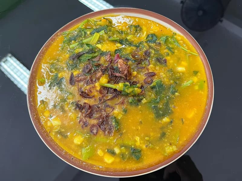 Semangkuk bubur Manado tinutuan kuning labu dengan jagung, sayuran hijau, dan taburan bawang goreng