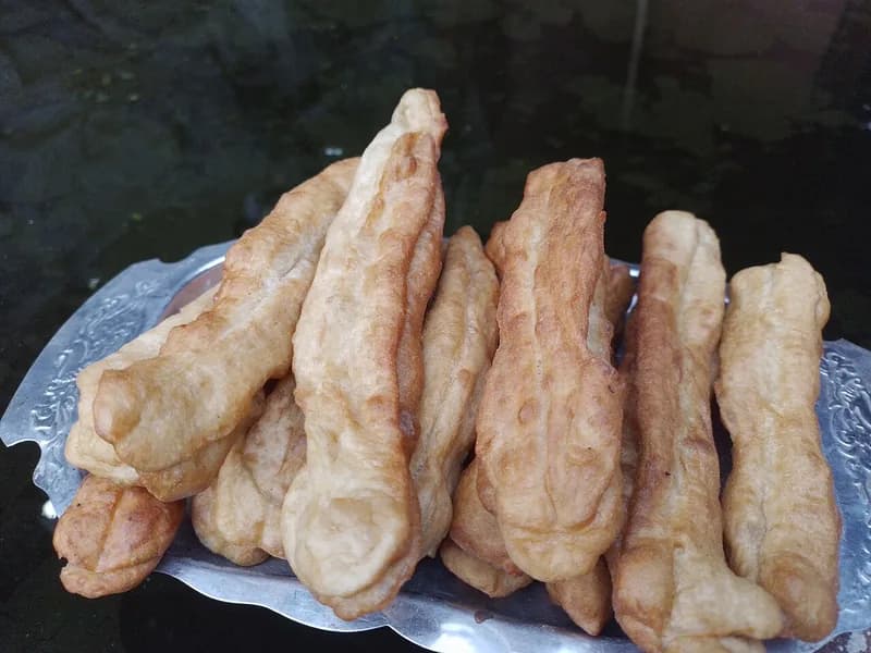 Tumpukan cakwe goreng panjang berwarna kuning kecokelatan di atas nampan aluminium