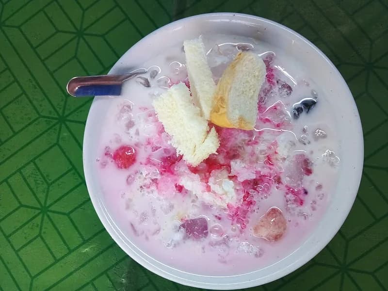 Semangkuk es campur dengan sirup merah muda, susu, jeli, kolang-kaling, dan potongan roti tawar