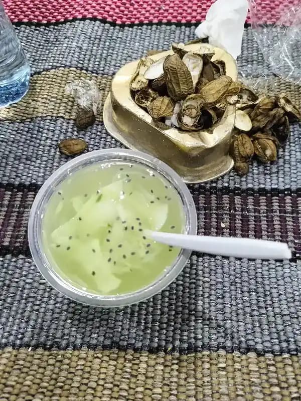 Semangkuk es kuwut hijau muda berisi serutan kelapa muda dan biji selasih dengan sendok plastik