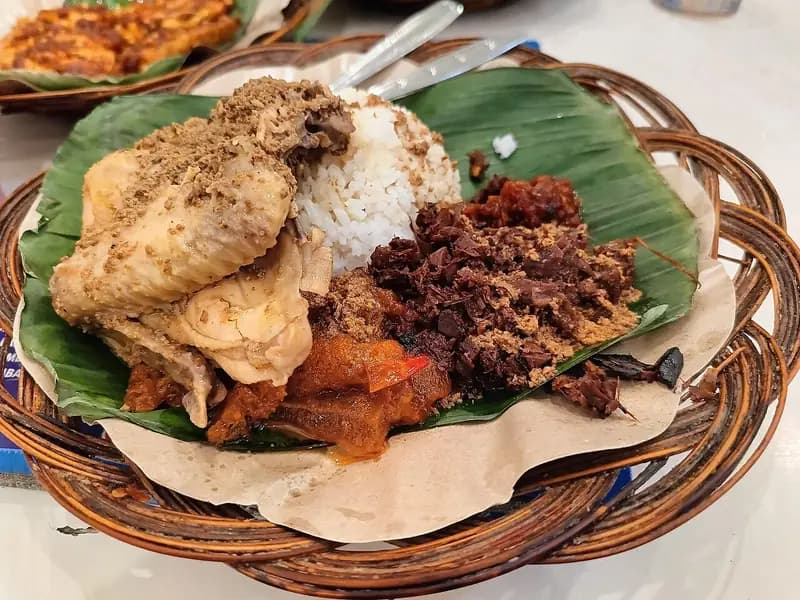 Nasi gudeg dengan ayam opor, krecek sambal, dan gudeg nangka cokelat di atas daun pisang