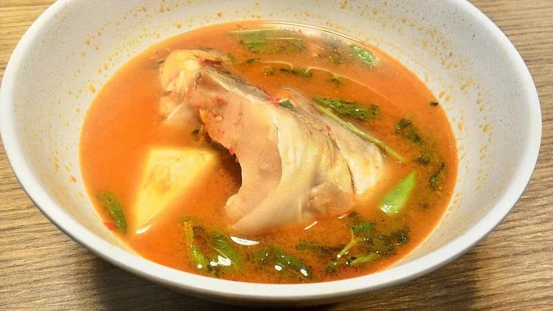 Semangkuk pindang ikan patin khas Palembang berkuah oranye dengan potongan nanas dan daun kemangi