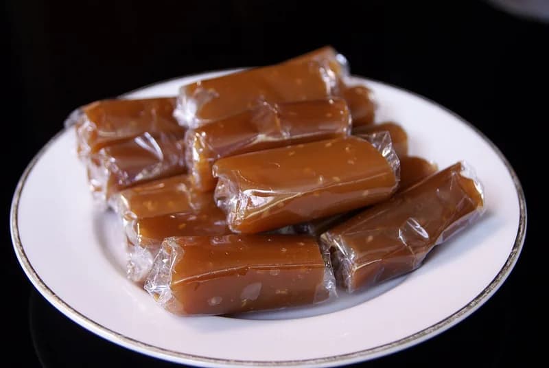 Potongan jenang Kudus cokelat legit terbungkus plastik bening di atas piring putih
