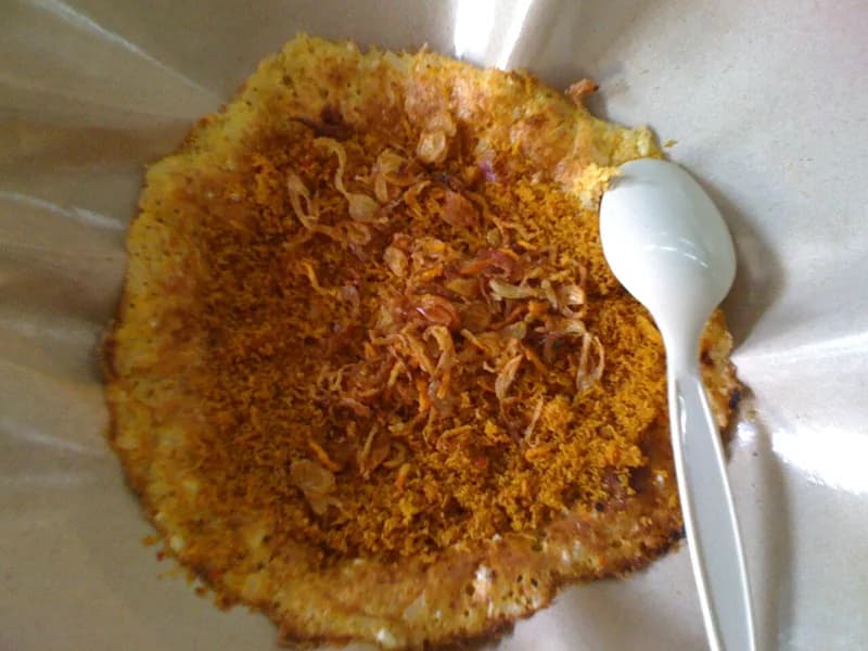 Kerak telor Betawi matang bertabur serundeng kelapa dan bawang goreng di atas kertas pembungkus