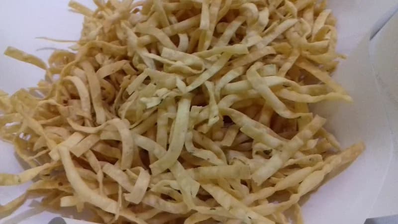 Tumpukan kue bawang berbentuk stik pipih kuning pucat dengan bintik daun seledri