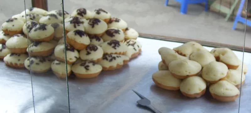 Tumpukan kue cubit berwarna kuning dengan taburan meses cokelat di etalase pedagang