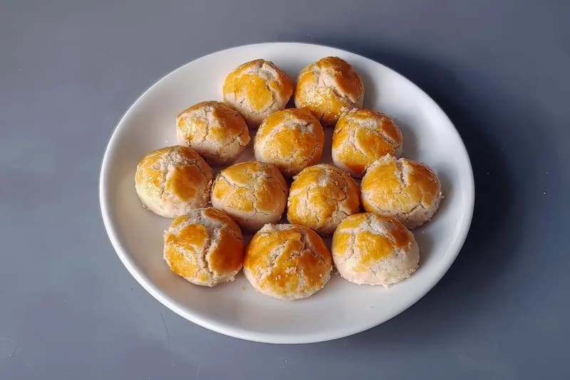 Kue kacang bulat berolesan kuning telur dengan permukaan retak tersusun di piring putih