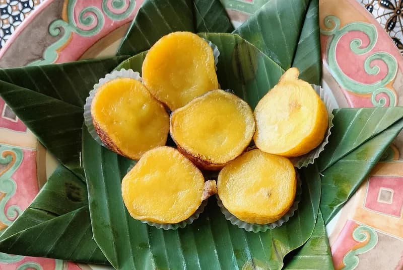 Enam kue lumpur kentang berwarna kuning keemasan dalam cup kertas di atas alas daun pisang