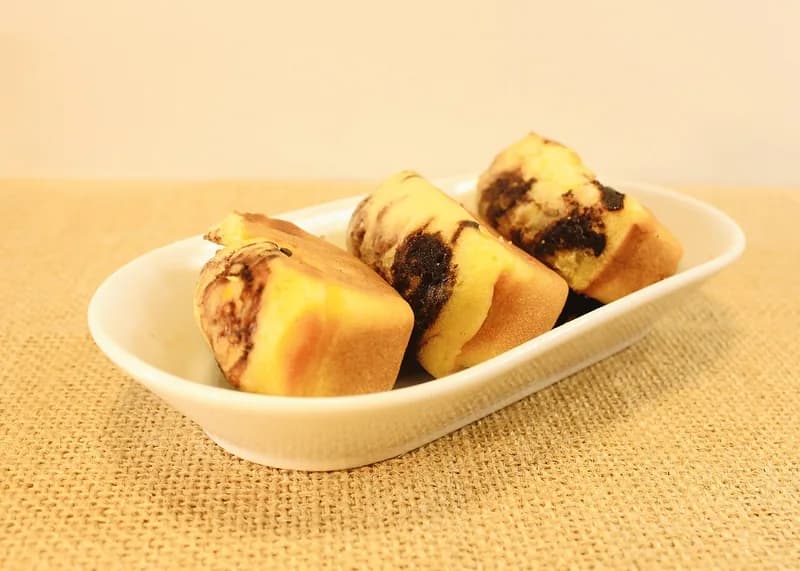 Tiga potong kue pukis kuning keemasan bertabur meses cokelat dalam piring oval putih