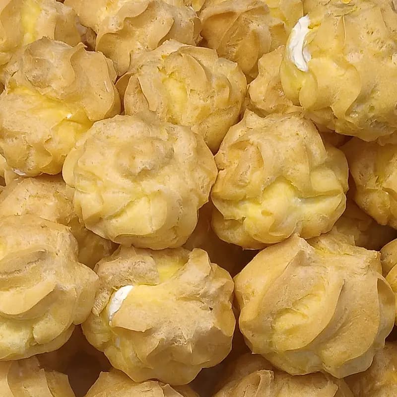 Tumpukan kue sus berkulit keemasan dengan isian vla kuning dan krim putih yang mengintip dari celah