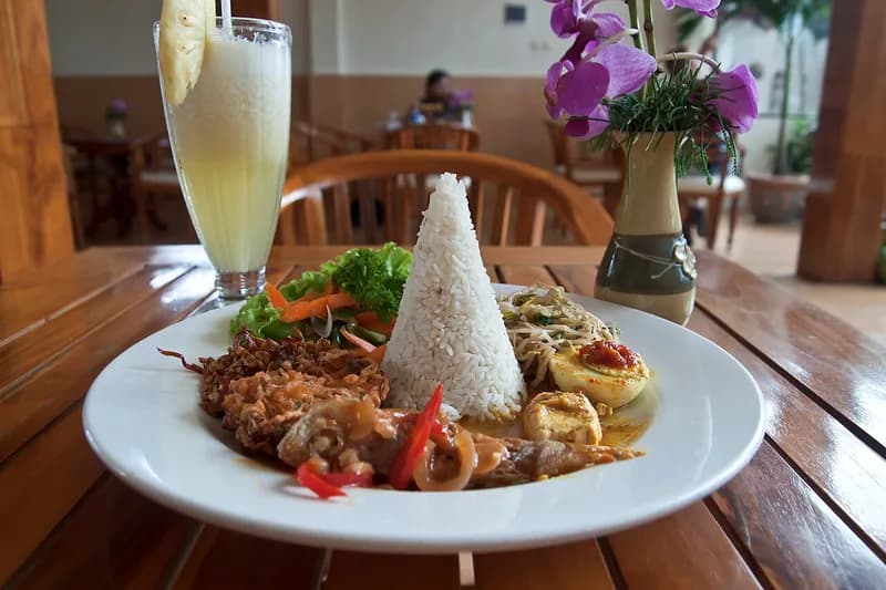 Sepiring nasi campur dengan nasi berbentuk kerucut, telur bumbu, sayuran, dan lauk tumis di meja kayu