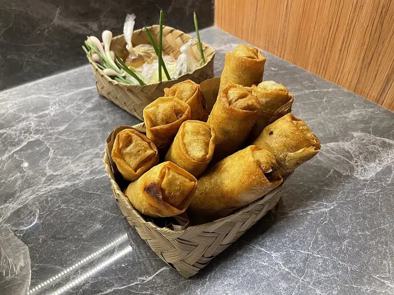 Lumpia Semarang goreng dalam besek bambu dengan daun bawang dan saus kental di wadah terpisah